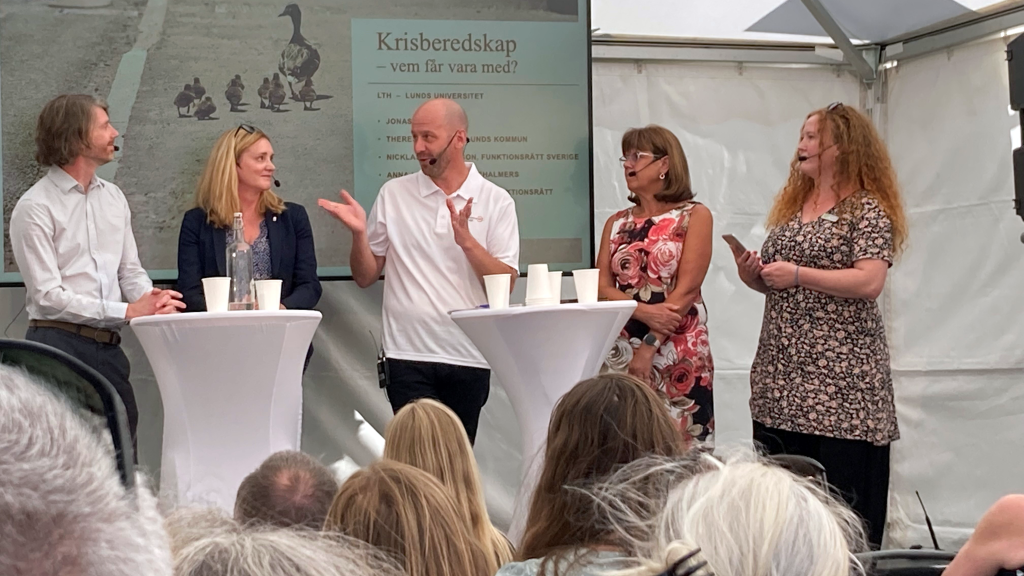Fem personer står och samtalar med varandra i ett tält