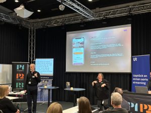 En person pekar mot en skärm i bakgrunden.