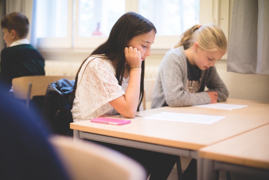 Två flickor sitter bredvid varandra i en skolbänk i ett klassrum
