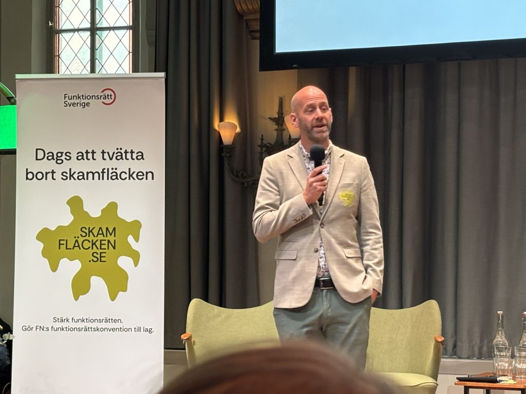En man i ljus kavaj talar i mikrofon