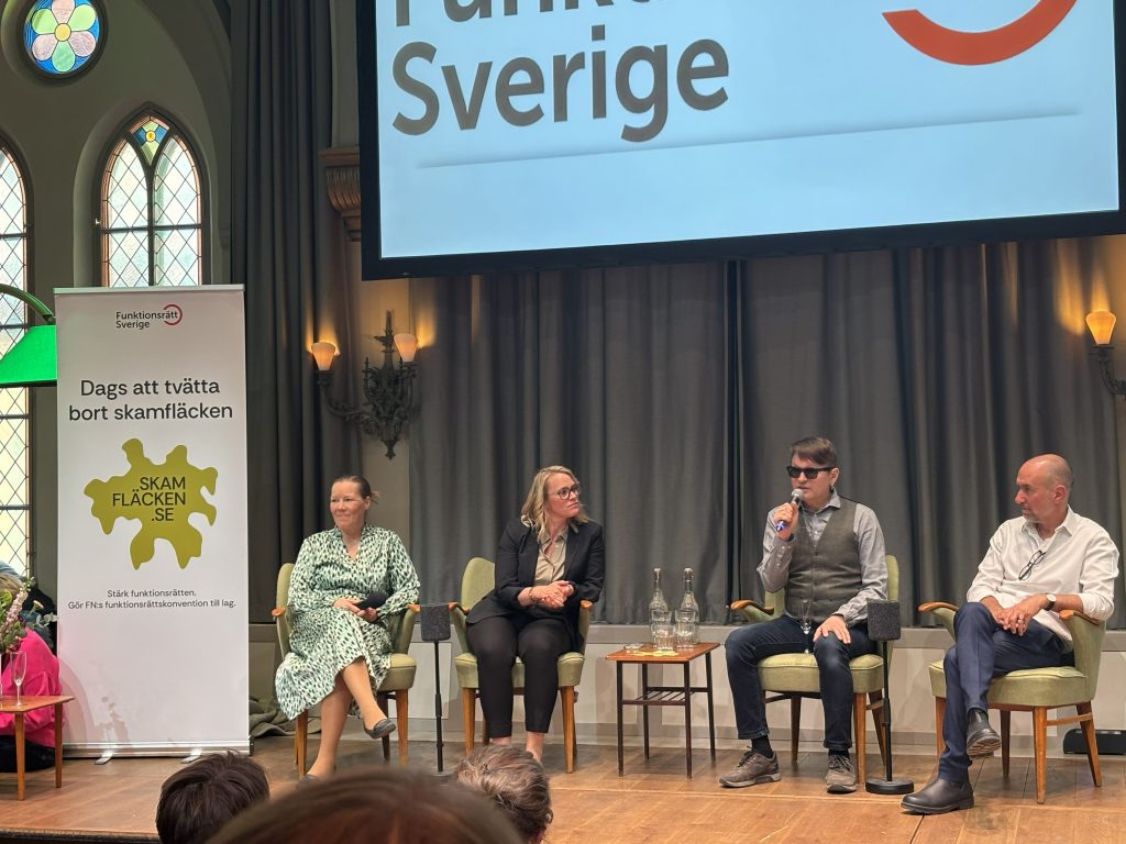 En panel med fyra personer som sitter på en scen.