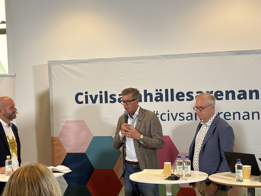 Tre män diskuterar i en panel
